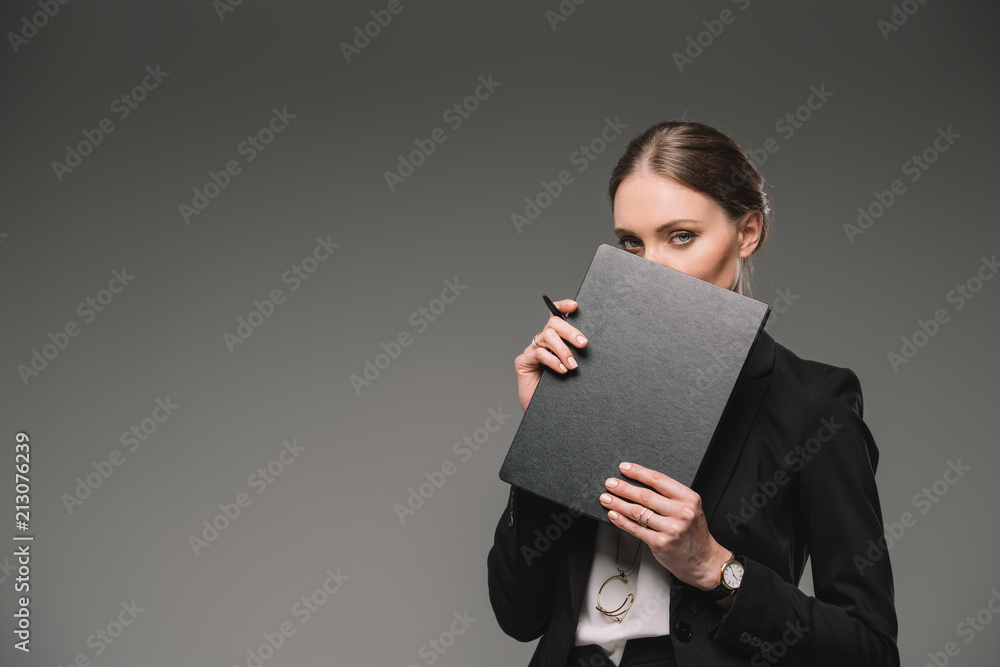businesswoman covering face by textbook isolated on grey background businesswoman covering face by textbook isolated on grey background