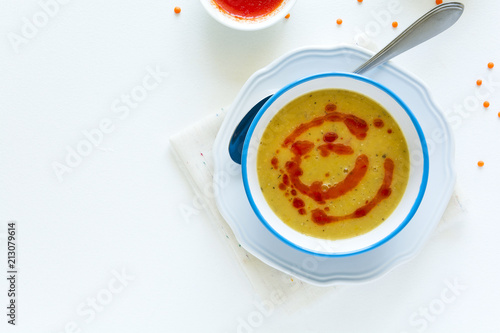 Red lentil soup with chili pepper sauce and bread on white wooden table