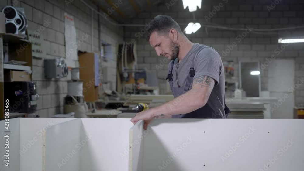 Working adult man in uniform making stand with white panels in garage Working adult man in uniform making stand with white panels in garage