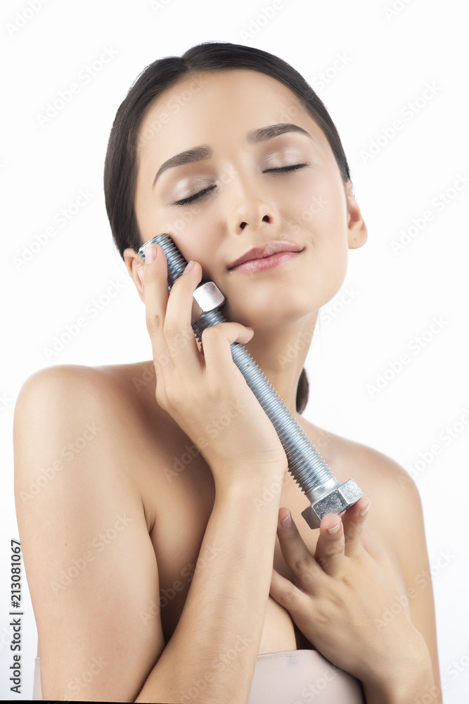 A beautiful smiling girl with naked shoulders puts the large steel bolt with a nut, which she holds in her hands to her face. Isolated on white A beautiful smiling girl with naked shoulders puts the large steel bolt with a nut, which she holds in her hands to her face. Isolated on white
