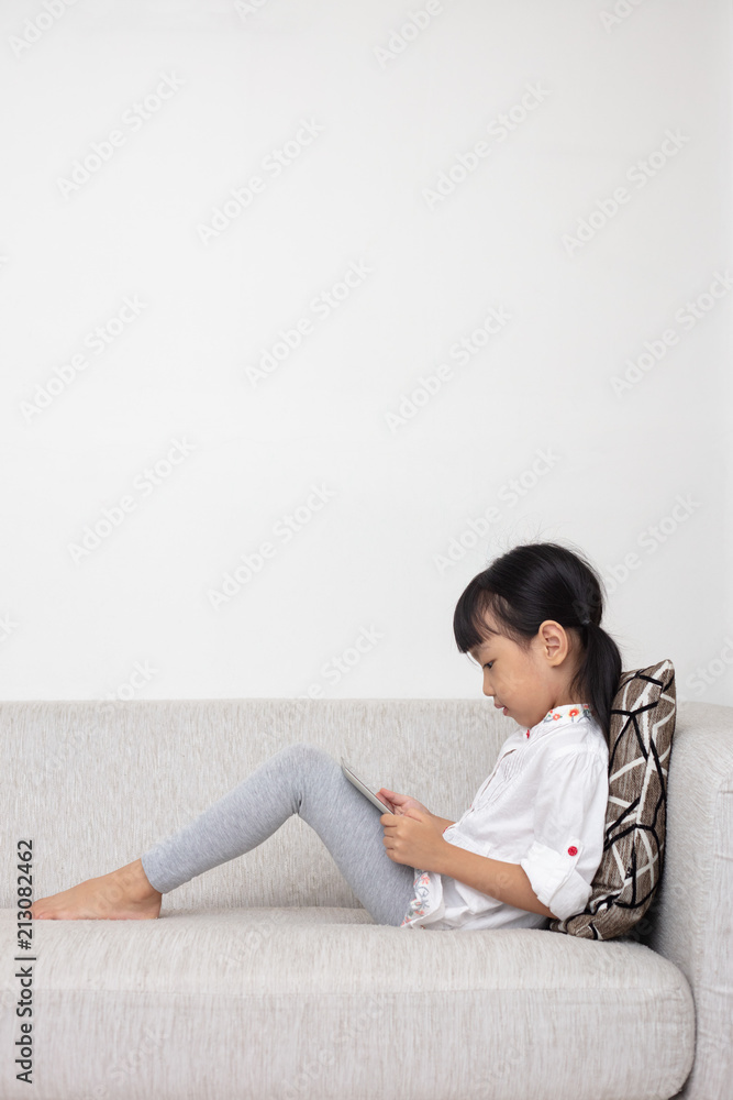 Asian Chinese little girl sitting on the sofa playing digital tablet Asian Chinese little girl sitting on the sofa playing digital tablet