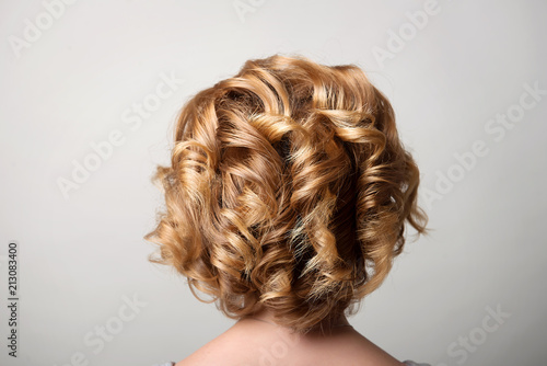 Hairstyle short curls on the head of a blonde view from behind.A woman s hairdo.