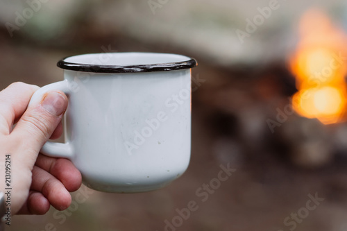 hands holding cup of tea the outdoors. Adventure, travel, tourism and camping concept. Hiker drinking tea from mug at camp