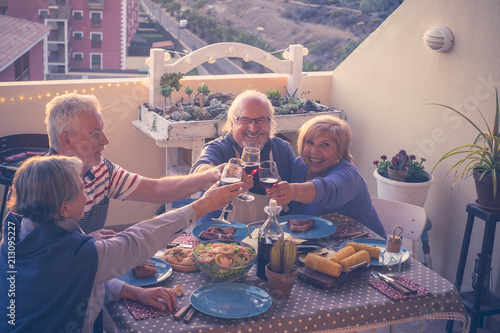 group of caucasian adult mature people eating and drinking together celebrating event by night on the rooftop with city and nature view. summer time and vacation concept for people photo