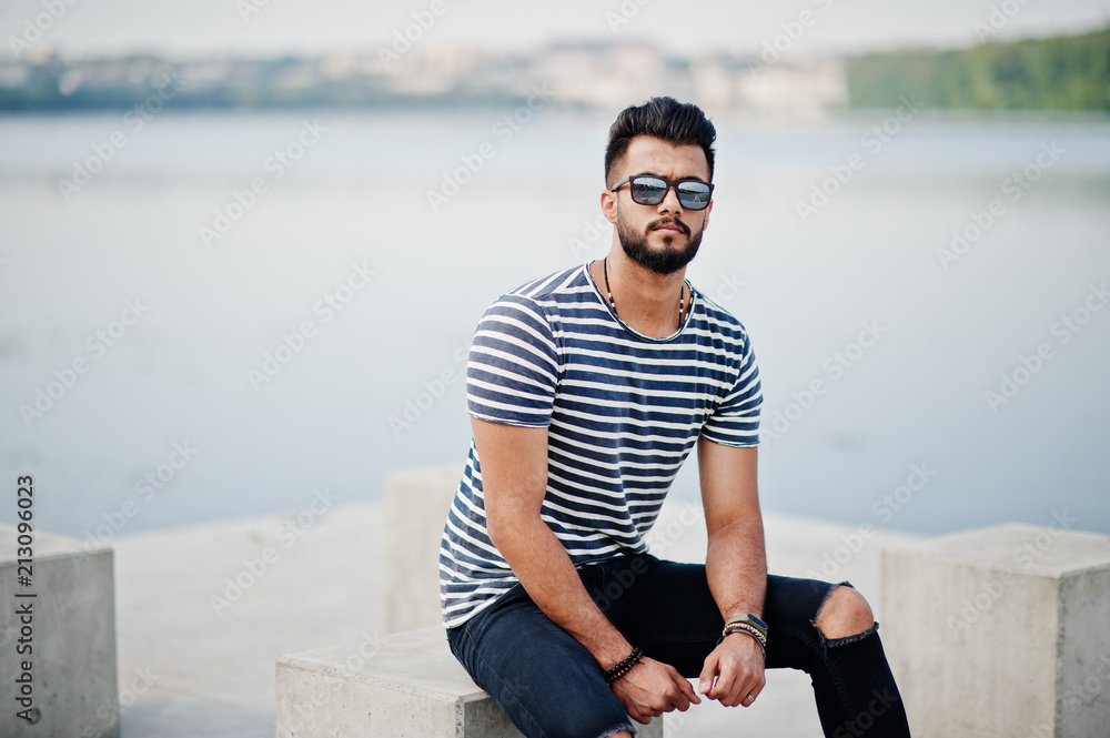 Handsome tall arabian beard man model at stripped shirt posed outdoor. Fashionable arab guy at sunglasses.