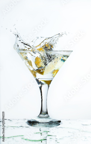 A glass of martini and slice of lemon, a splash and spray on a light background