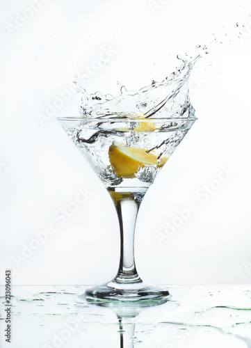 A glass of martini and slice of lemon, a splash and spray on a light background