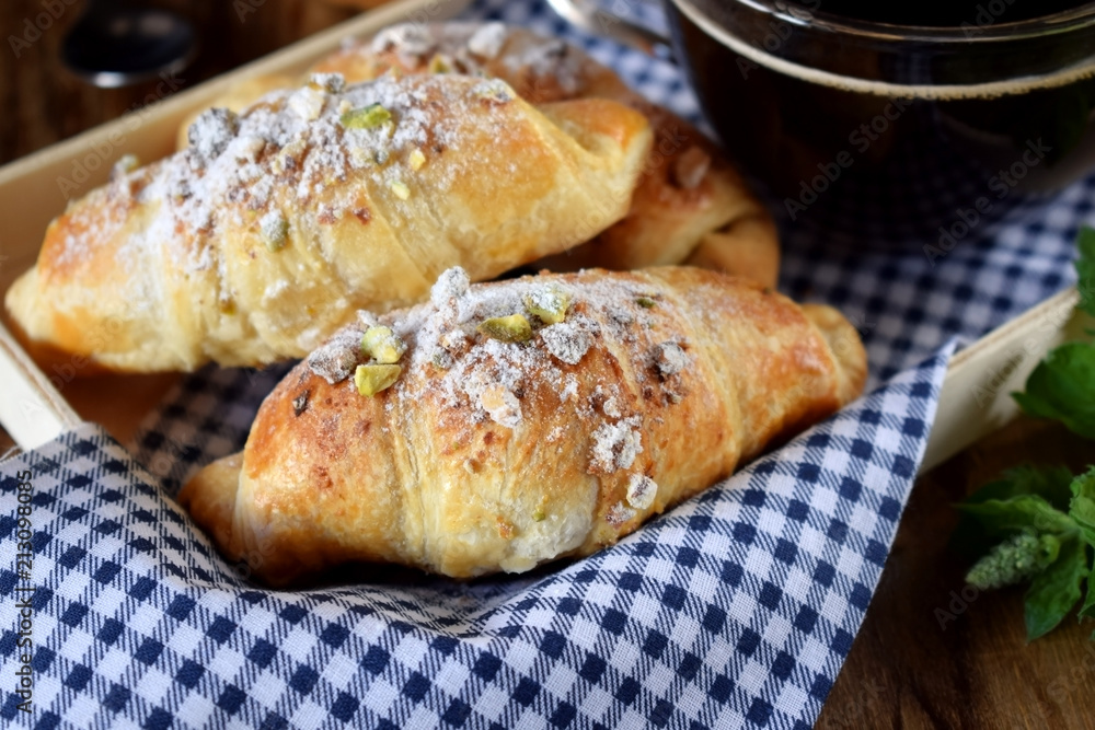 Fresh croissants sprinkled with nuts and a cup of black coffee