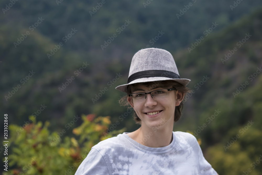 Cute young teenager in a hat smiles happily against the background of a mountain nature.