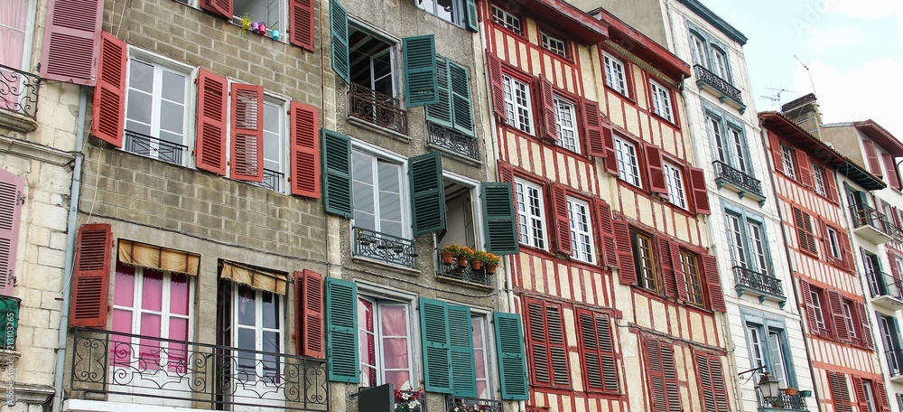 Facade of colorful houses with green and red wood windows. Small balconies in the city of Bayonne, South of France