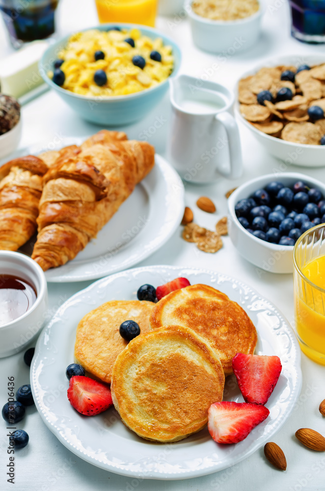Breakfast table setting with flakes, juice, croissants, pancakes and fresh berries Breakfast table setting with flakes, juice, croissants, pancakes and fresh berries
