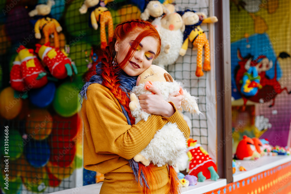young cheerful red-haired girl posing in the amusement Park. Portrait of a woman with bright makeup and long red hair. She poses, has fun and plays. young cheerful red-haired girl posing in the amusement Park. Portrait of a woman with bright makeup and long red hair. She poses, has fun and plays.