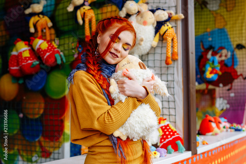 young cheerful red-haired girl posing in the amusement Park. Portrait of a woman with bright makeup and long red hair. She poses, has fun and plays.