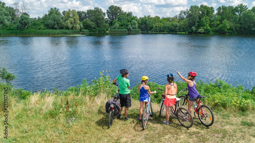 Family on bikes cycling outdoors, active parents and kids on bicycles, aerial view of happy family with children relaxing near beautiful river from above, sport and fitness concept 