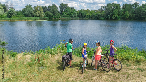 Family on bikes cycling outdoors, active parents and kids on bicycles, aerial view of happy family with children relaxing near beautiful river from above, sport and fitness concept
