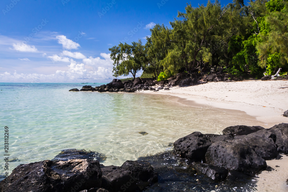 blue ocean and black lava stones on a sandy beach of volcanic island Mauritius