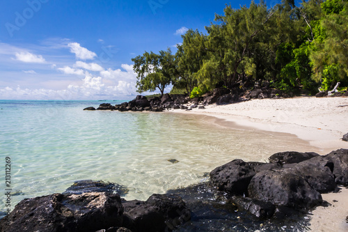 blue ocean and black lava stones on a sandy beach of volcanic island Mauritius