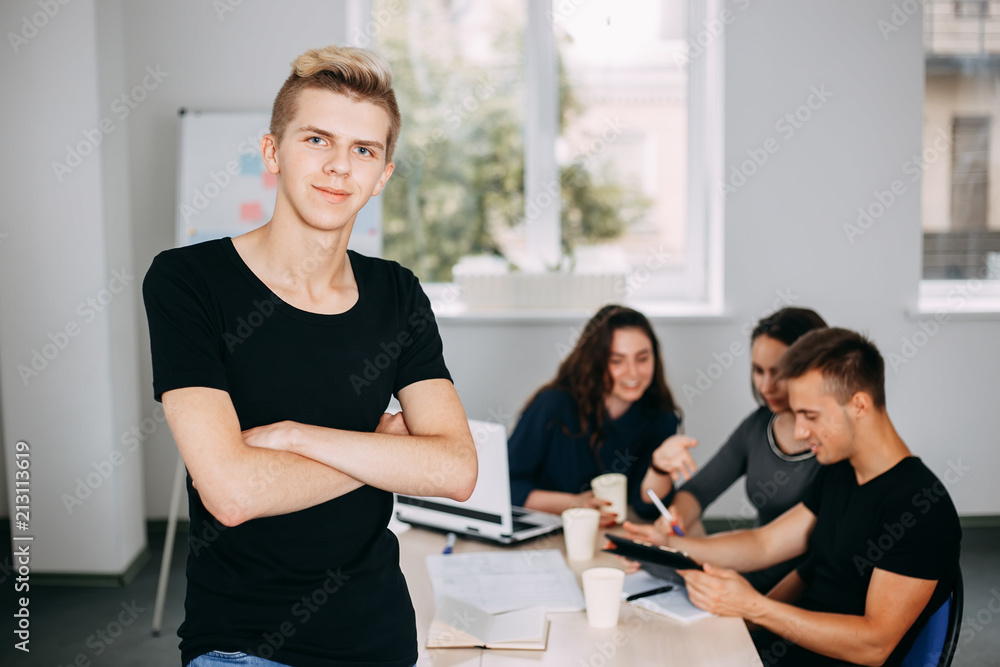 Fototapeta premium I am the part of cohesive team. Young successful man specialist portrait with colleagues meeting behind him. friendly atmosphere, communication and comradery