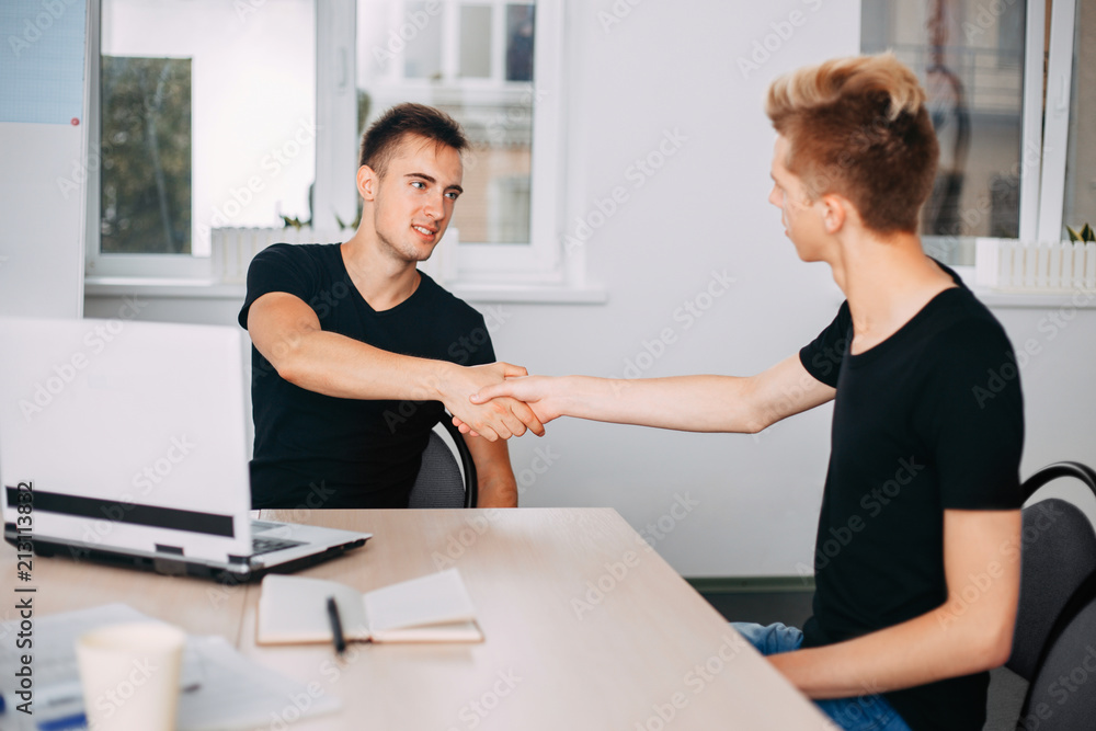 hiring new team member, celebrating success. Young modern men shaking hands while working in the creative office hiring new team member, celebrating success. Young modern men shaking hands while working in the creative office