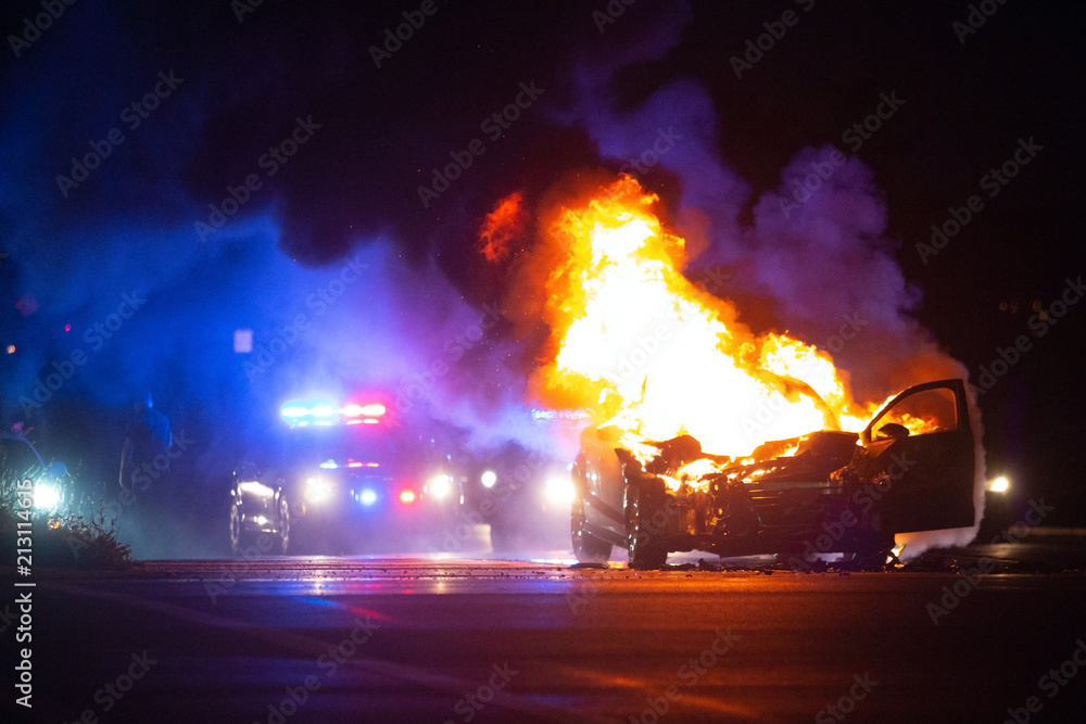 Car on fire at night with police lights in background