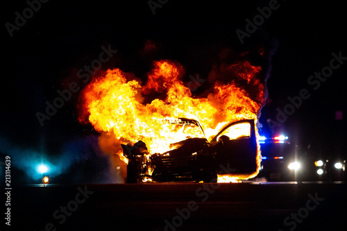 Car on fire at night with police lights in background © PhotoSpirit