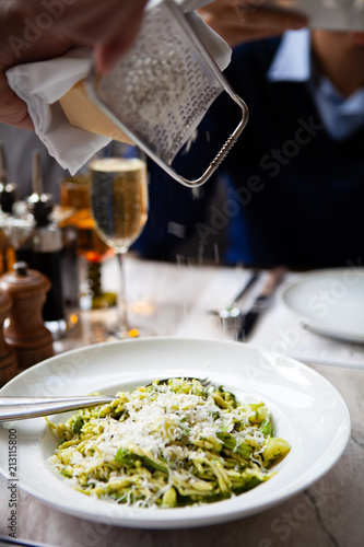Hands of a chef grated parmesan cheese on a traditional handmade Ligurian Pasta Trofie with fresh Pesto alla Genovese sauce . Natural light. photo