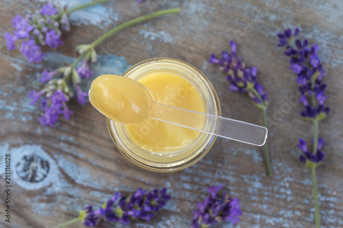 organic royal jelly in a glass bottle and full spoon with lavender decoration over the jar on wooden board photo