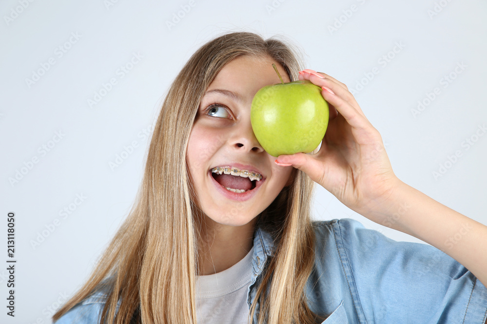 Young smiling girl with dental braces and green apple on grey background Young smiling girl with dental braces and green apple on grey background