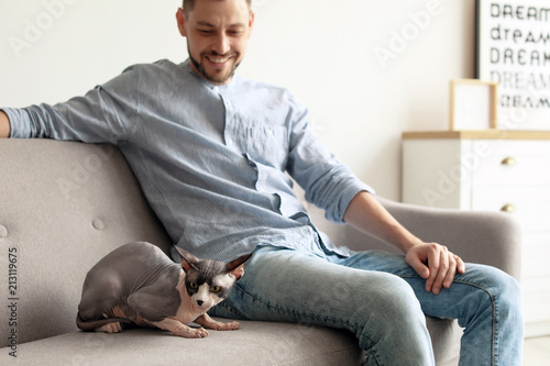 Young man with cute cat on sofa at home © New Africa