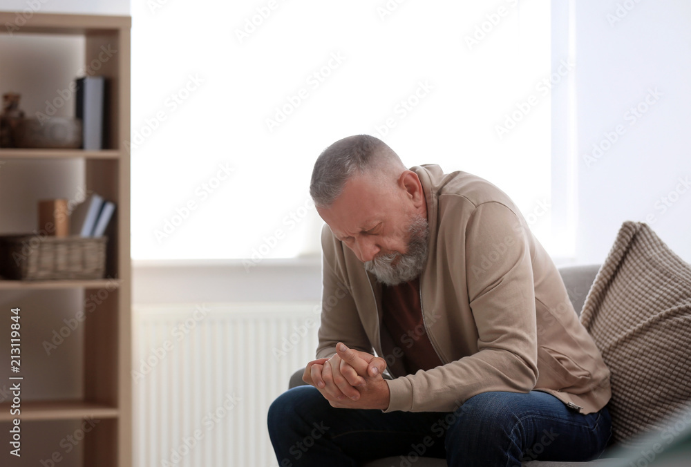 Depressed senior man sitting on sofa indoors