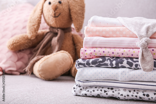Stack of stylish child clothes and toy bunny on couch © New Africa
