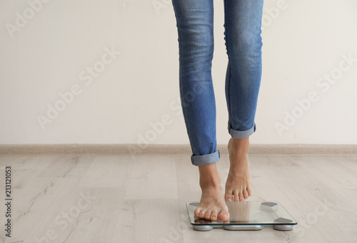 Woman measuring her weight using scales on wooden floor. Healthy diet