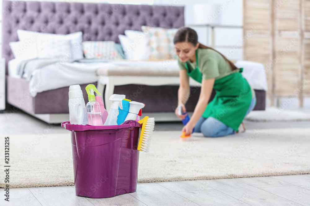 Bucket with cleaning supplies and woman in uniform on background Bucket with cleaning supplies and woman in uniform on background