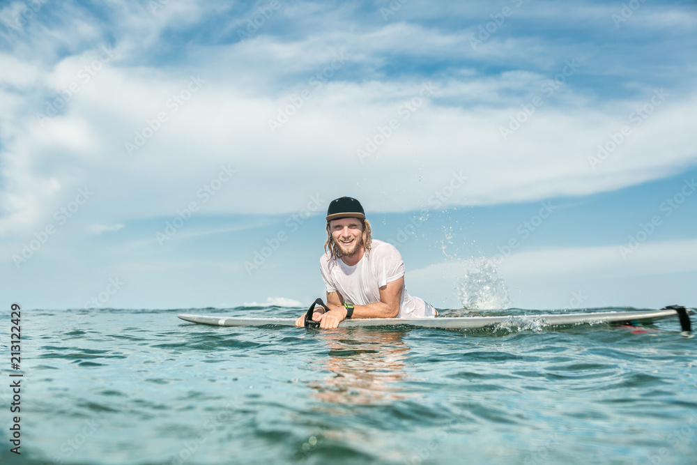 smiling male surfer resting in ocean with surfing board at Nusa Dua Beach, Bali, Indonesia