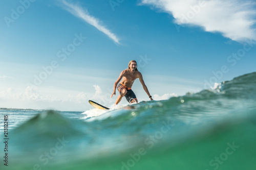 surface level of shirtless male surfer riding waves in ocean at Nusa Dua Beach, Bali, Indonesia