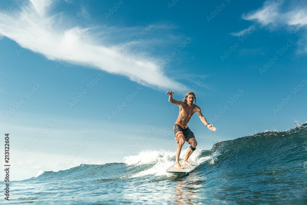handsome shirtless male surfer riding waves in ocean at Nusa Dua Beach, Bali, Indonesia