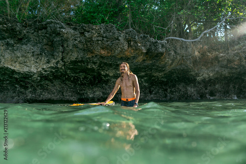 surface level of shirtless smiling male surfer standing in ocean with surfing board in Bali, Indonesia © LIGHTFIELD STUDIOS