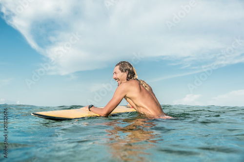 side view of smiling shirtless male surfer swimming with surfing board in ocean at Nusa Dua Beach  Bali  Indonesia
