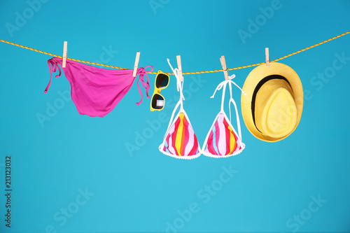 Beautiful bikini, hat and sunglasses hanging on rope against color background