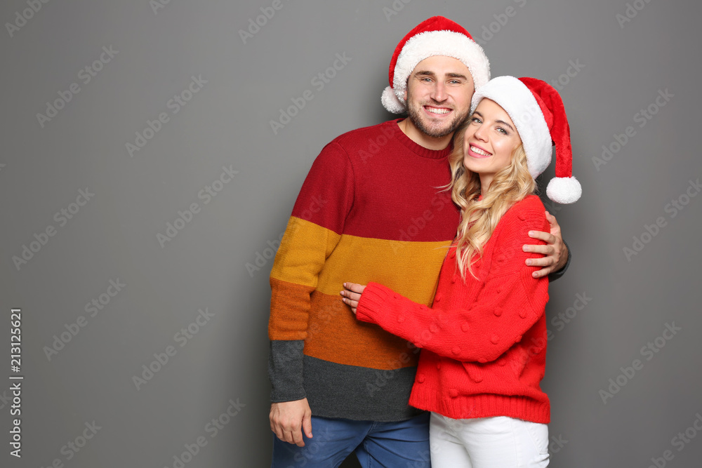 Young couple in Santa hats on grey background. Christmas celebration Young couple in Santa hats on grey background. Christmas celebration