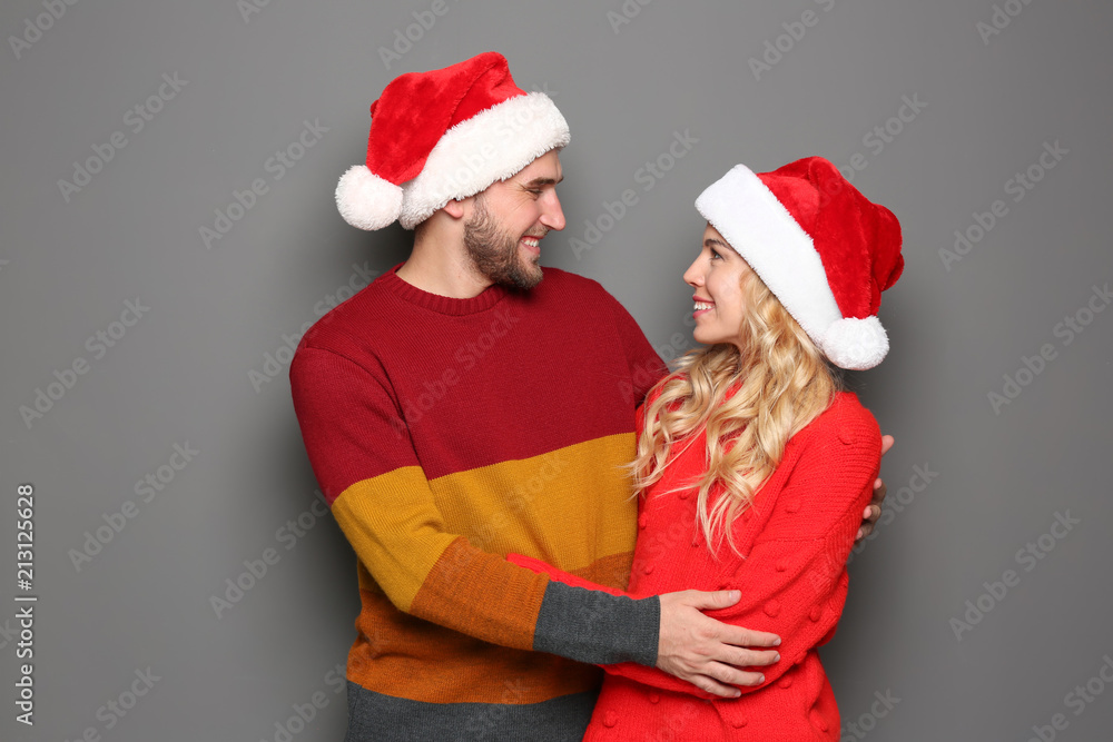 Young couple in Santa hats on grey background. Christmas celebration Young couple in Santa hats on grey background. Christmas celebration