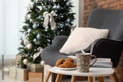 Book with treat on table and Christmas tree in stylish living room interior