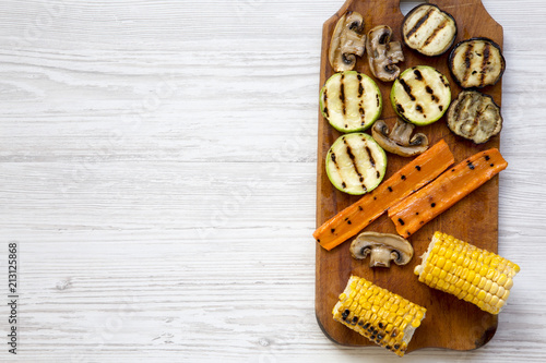 Grilled vegetables on rustic wooden board on a white wooden background, top view. From above, flat lay, overhead. Copy space and text area.