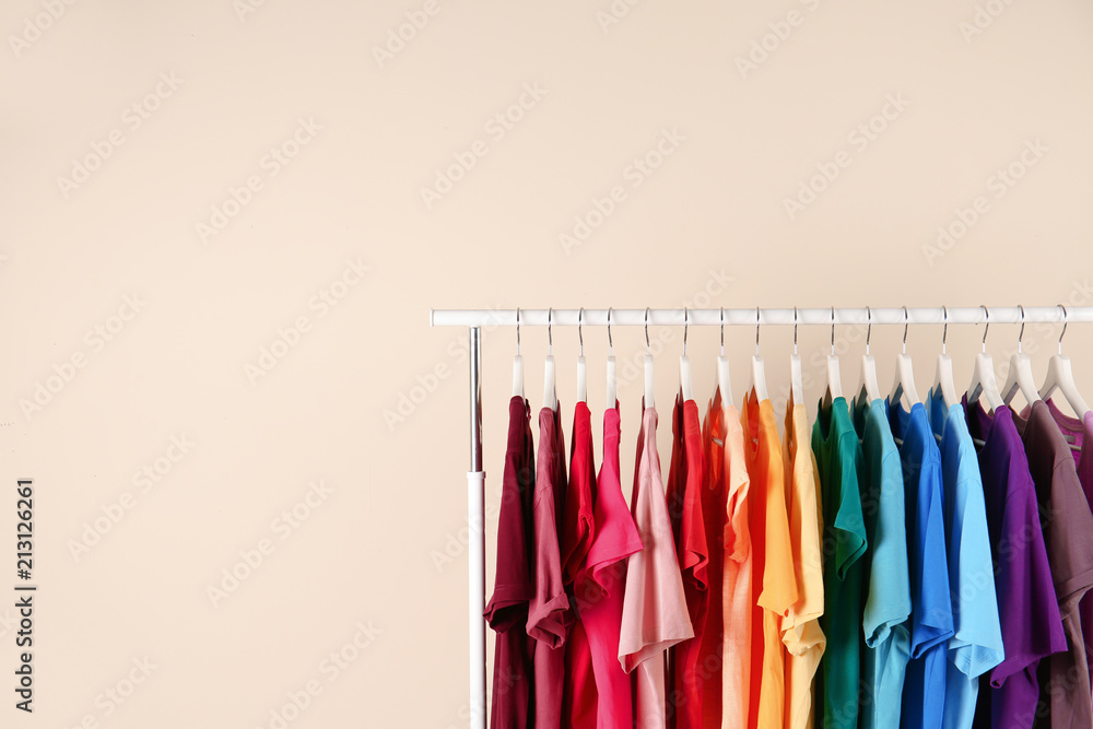 Many t-shirts hanging in order of rainbow colors on light background