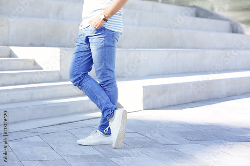 Young hipster man in stylish jeans standing near stairs outdoors