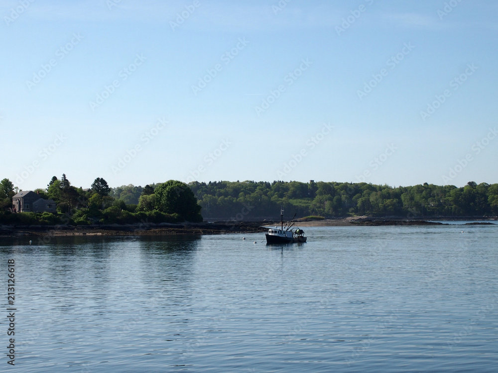 Fishing boat rests in water of Casco Bay off shore of island with house and trees