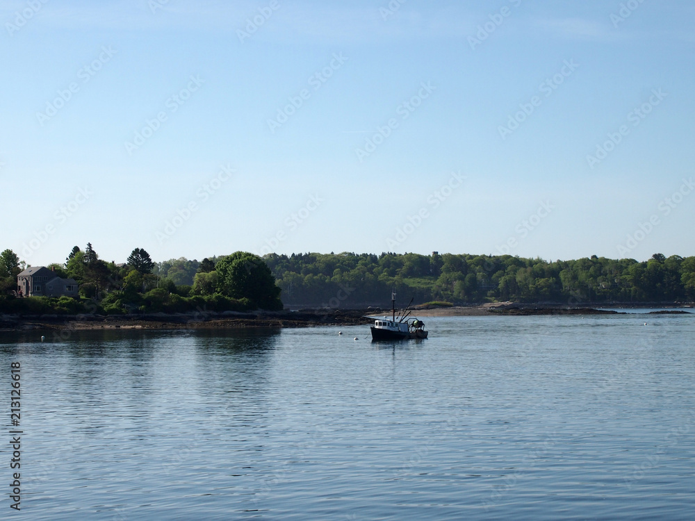 Fishing boat rests in water of Casco Bay off shore of island with house and trees Fishing boat rests in water of Casco Bay off shore of island with house and trees