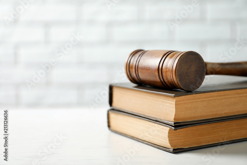 Wooden gavel and books on table against brick wall. Law concept