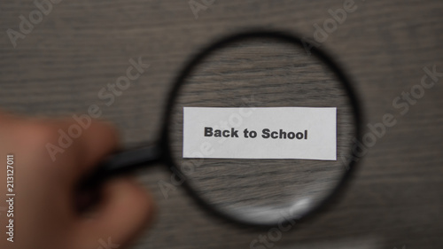 hand with a magnifying glass on a wooden background. Magnifier enlarges the phrase back to school. Concept of the school