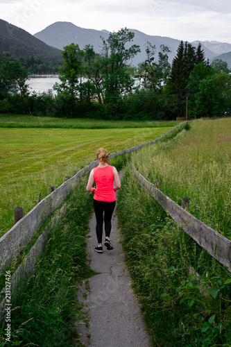 Young woman running along fenced path through field